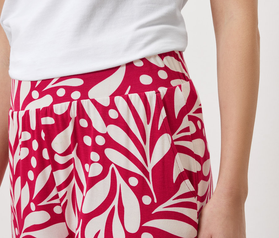 Gros plan d'une personne portant un t-shirt blanc et un pantalon rouge avec un motif de feuilles blanches.