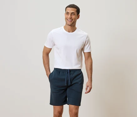 Homme portant un t-shirt blanc et un short bleu avec les mains dans les poches