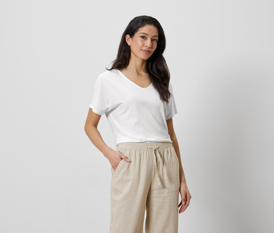 Femme portant un t-shirt blanc et un pantalon beige, une main dans la poche.
