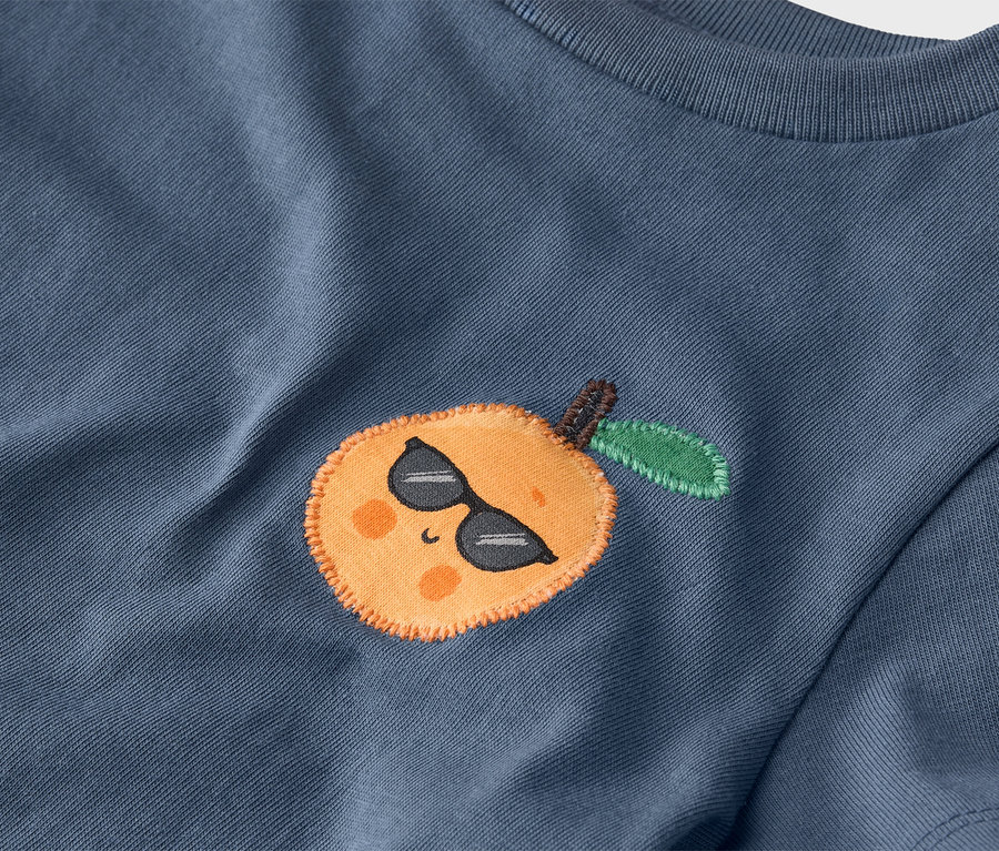 Gros plan d'un t-shirt bleu avec une mandarine cousue portant des lunettes de soleil.