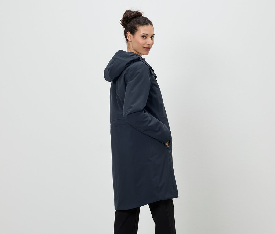Femme avec un chignon portant un long manteau de pluie bleu marine à capuche et un pantalon noir.