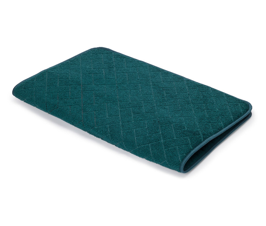 Une seule serviette turquoise foncé avec un motif géométrique en relief posée sur une surface blanche.