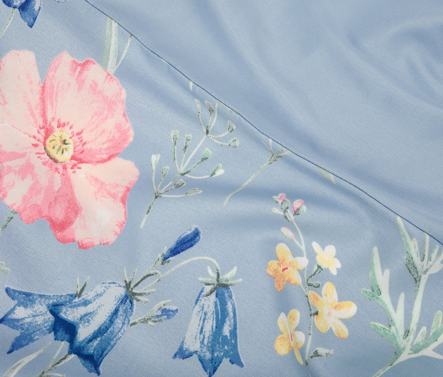 Gros plan d'un tissu bleu clair avec des coquelicots roses et des campanules bleues.