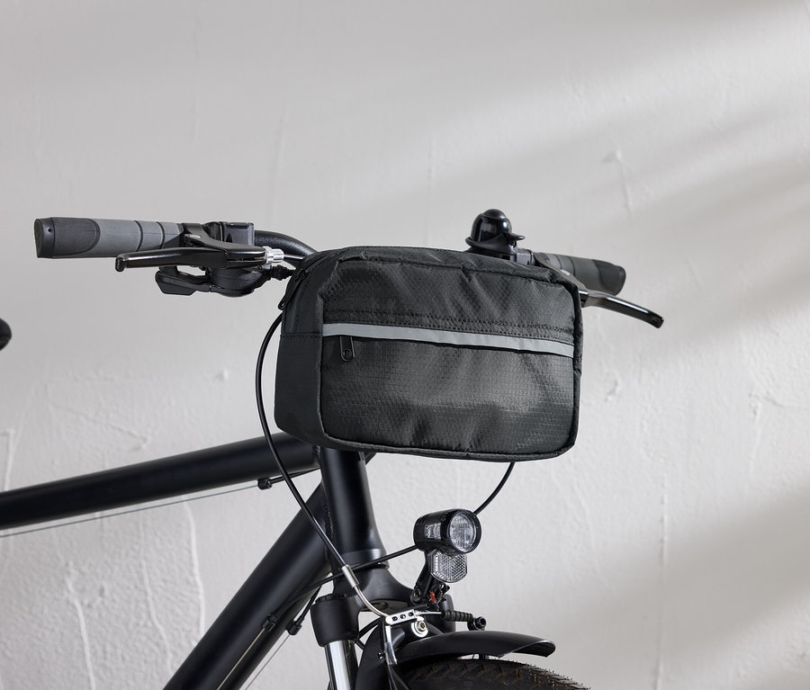 Vue détaillée d'un vélo noir avec une sacoche de guidon noire et un phare de vélo devant un mur blanc.