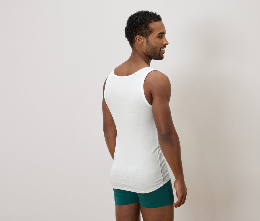 Homme vu de dos, portant un maillot de corps blanc et un boxer vert, regardant sur le côté.