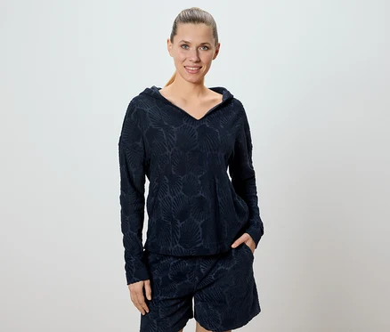 Une femme porte un ensemble sweat à capuche et short bleu marine avec un motif de coquillages.