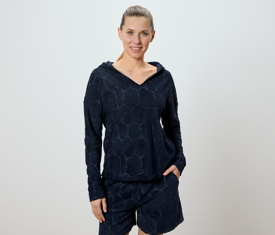 Une femme porte un ensemble sweat à capuche et short bleu marine avec un motif de coquillages.
