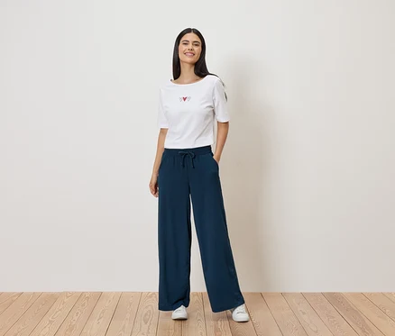 Une femme porte un t-shirt blanc avec un motif de cœur et un pantalon ample bleu marine à cordon de serrage. Elle porte des baskets blanches.