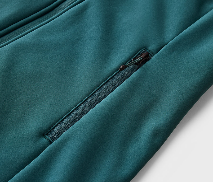 Gros plan d'une veste vert émeraude avec une poche zippée et une autre fermeture éclair en haut à gauche.