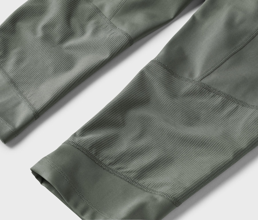 Gros plan sur des jambes de pantalon vert olive avec des empiècements texturés sur un fond neutre.