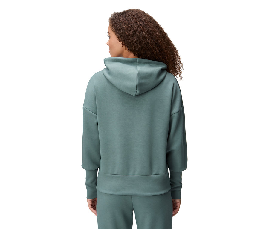 Vue arrière d'une femme aux cheveux bouclés portant un sweat à capuche vert et un pantalon assorti.