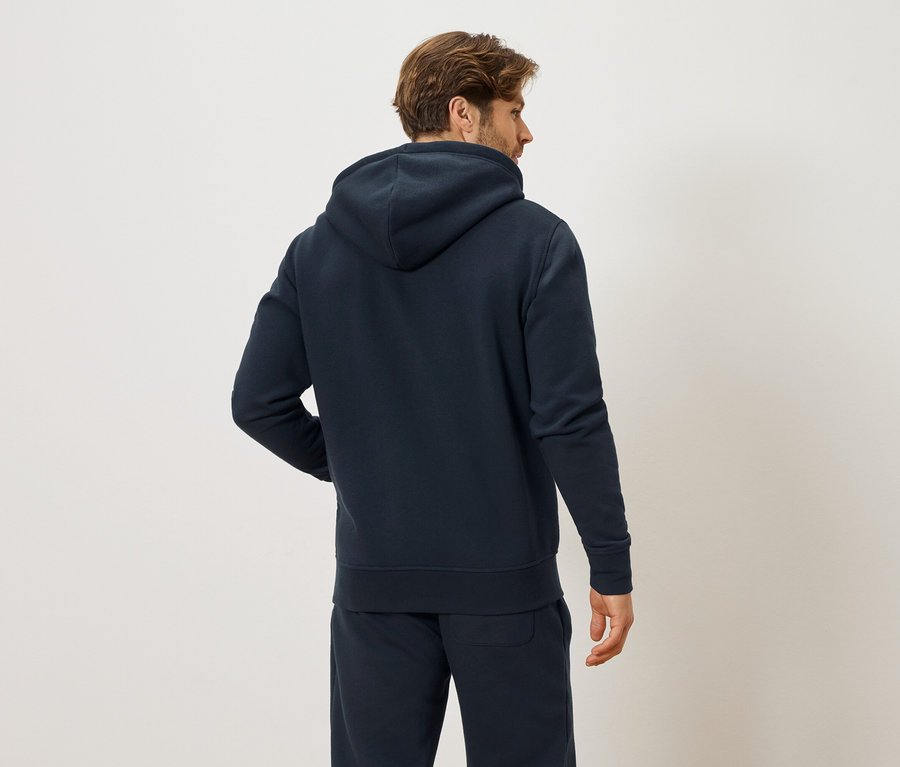 Vue arrière d'un homme aux cheveux bruns portant un sweat à capuche bleu marine et un pantalon de survêtement bleu marine.