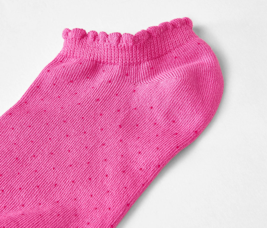 Gros plan d'une seule socquette rose à coupe basse avec bordure à froufrous et petits pois sur fond blanc.