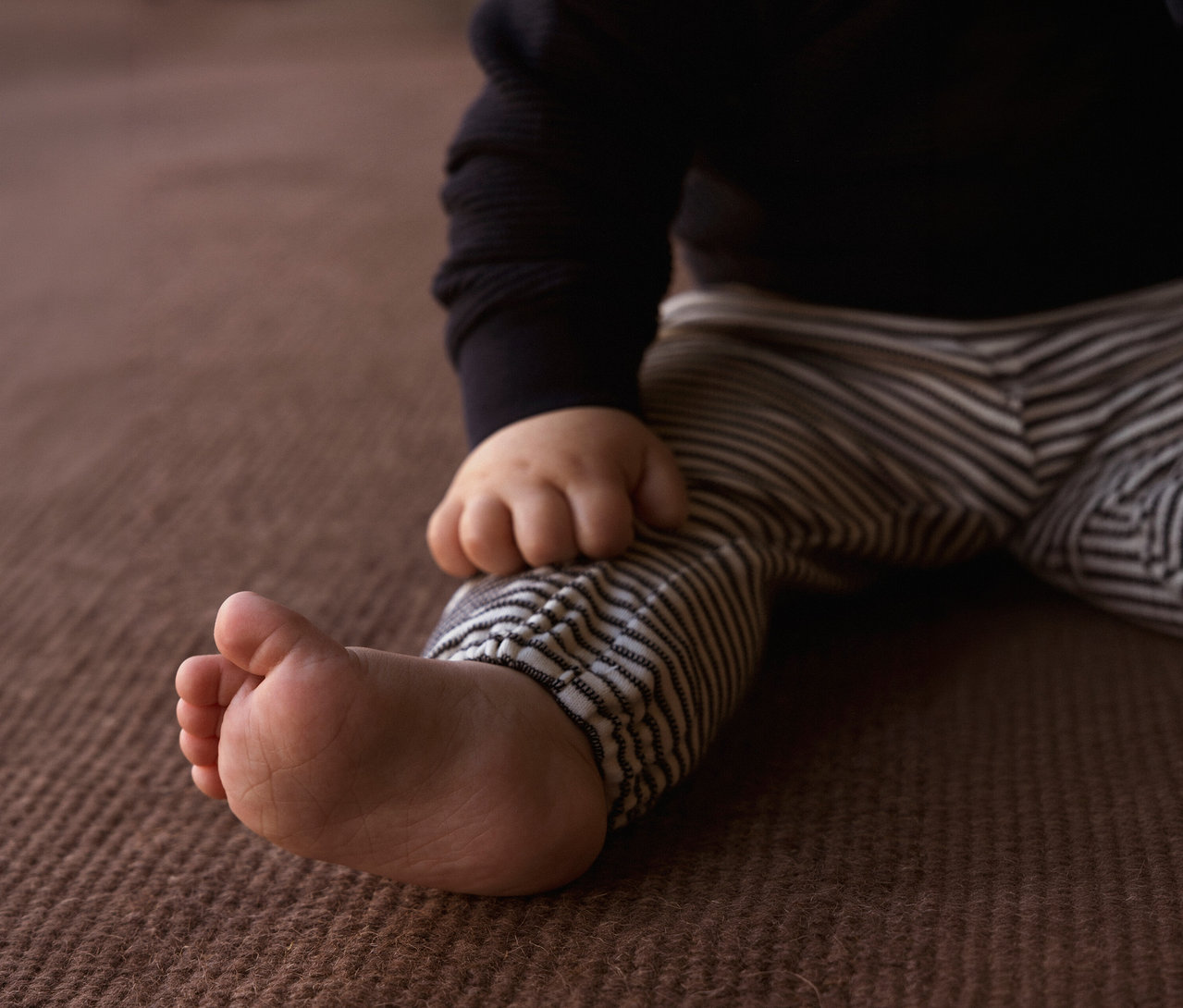 Gros plan sur un bébé portant un cardigan noir et un pantalon en jersey bébé NAME IT rayé.