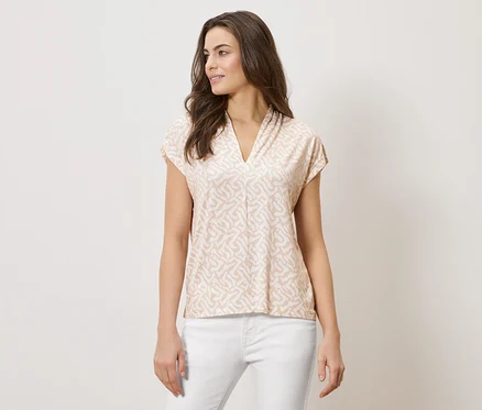 Femme portant un haut imprimé marron clair à col en V et un pantalon blanc.