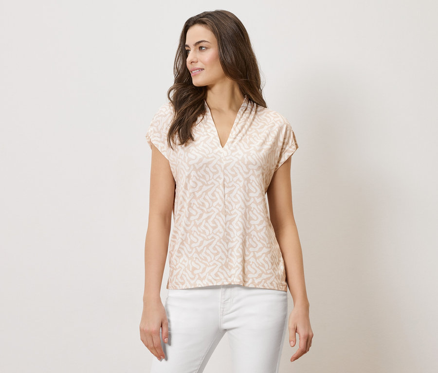 Femme portant un haut imprimé marron clair à col en V et un pantalon blanc.