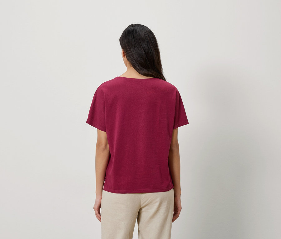 Vue de dos d'une femme aux longs cheveux foncés portant un t-shirt bordeaux et un pantalon beige.