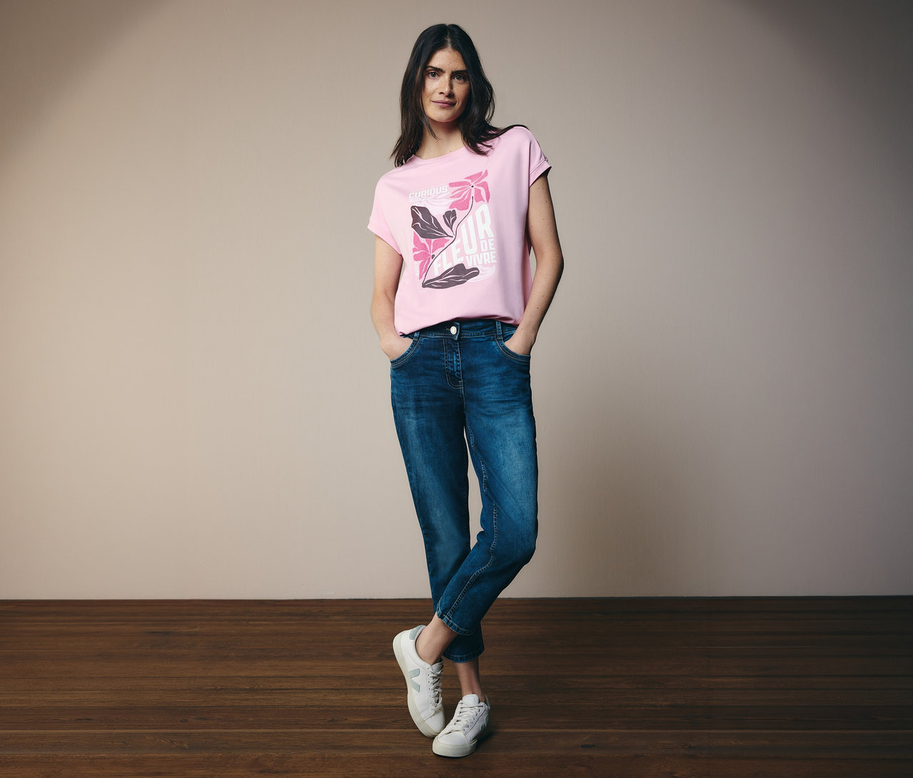 Une femme en jean et baskets porte un T-shirt à motif CECIL rose avec un imprimé floral.