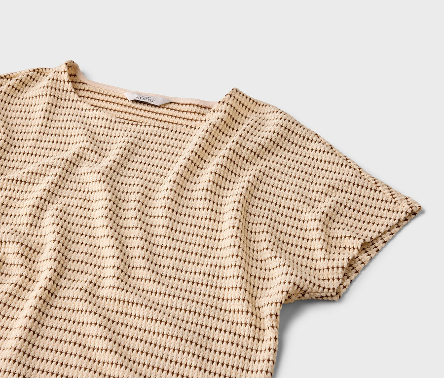 Gros plan d'un haut à manches courtes beige avec un motif à pois marron sur fond gris.