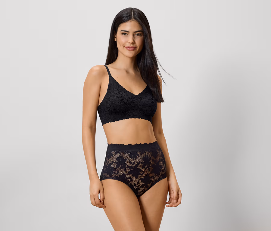 Femme portant un soutien-gorge en dentelle noire et une culotte taille haute sur fond clair.