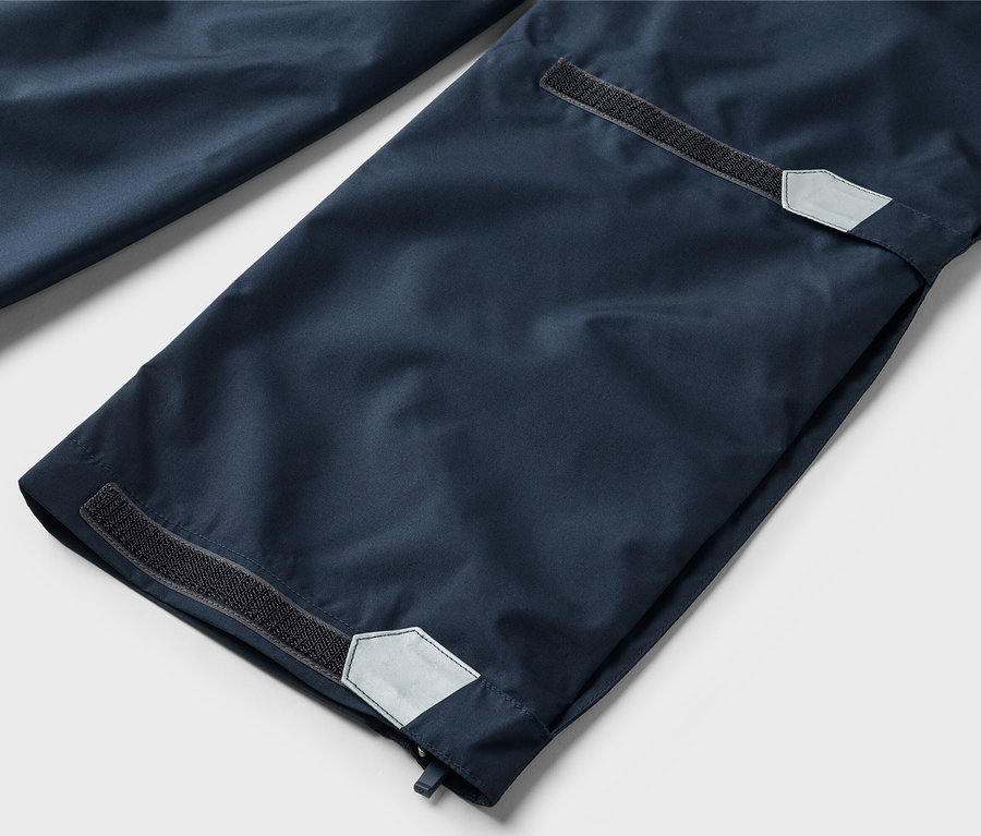 Gros plan sur des bas de pantalon bleu marine avec fermeture velcro et détails réfléchissants sur les ourlets.