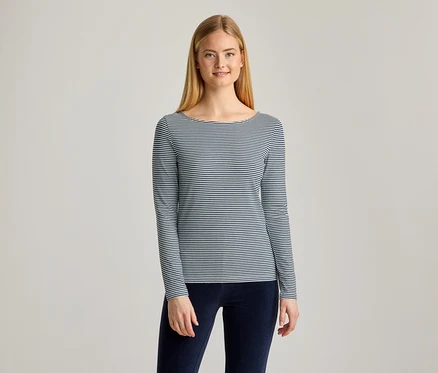 Jeune femme aux longs cheveux blonds, souriante, portant un haut rayé à manches longues et col bateau, et un pantalon bleu foncé.