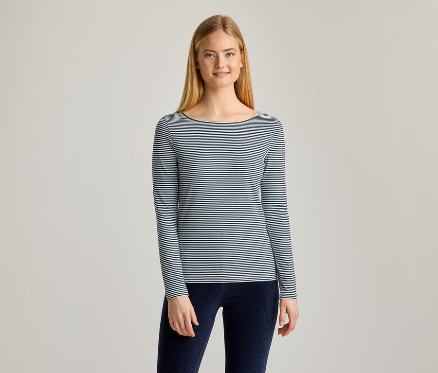 Jeune femme aux longs cheveux blonds, souriante, portant un haut rayé à manches longues et col bateau, et un pantalon bleu foncé.