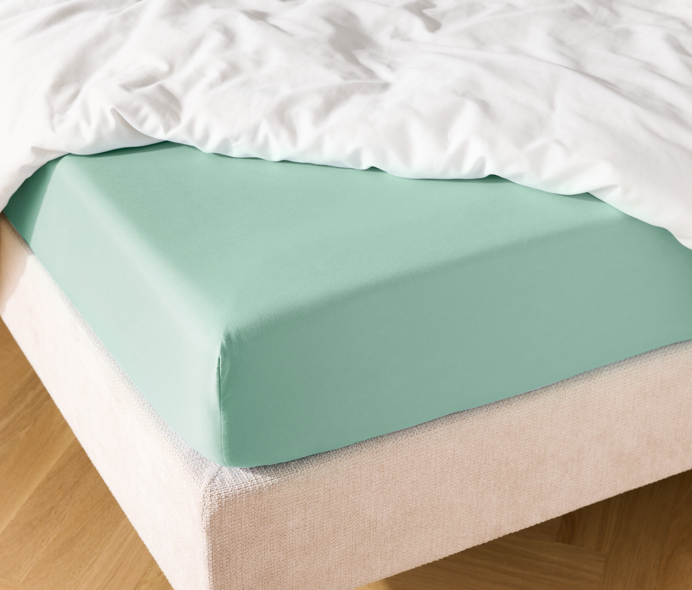 Lit avec drap-housse vert menthe et couette blanche.
