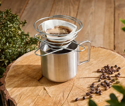 Du café est versé dans une tasse en acier inoxydable sur une souche d'arbre à l'aide d'un porte-filtre à café en spirale.