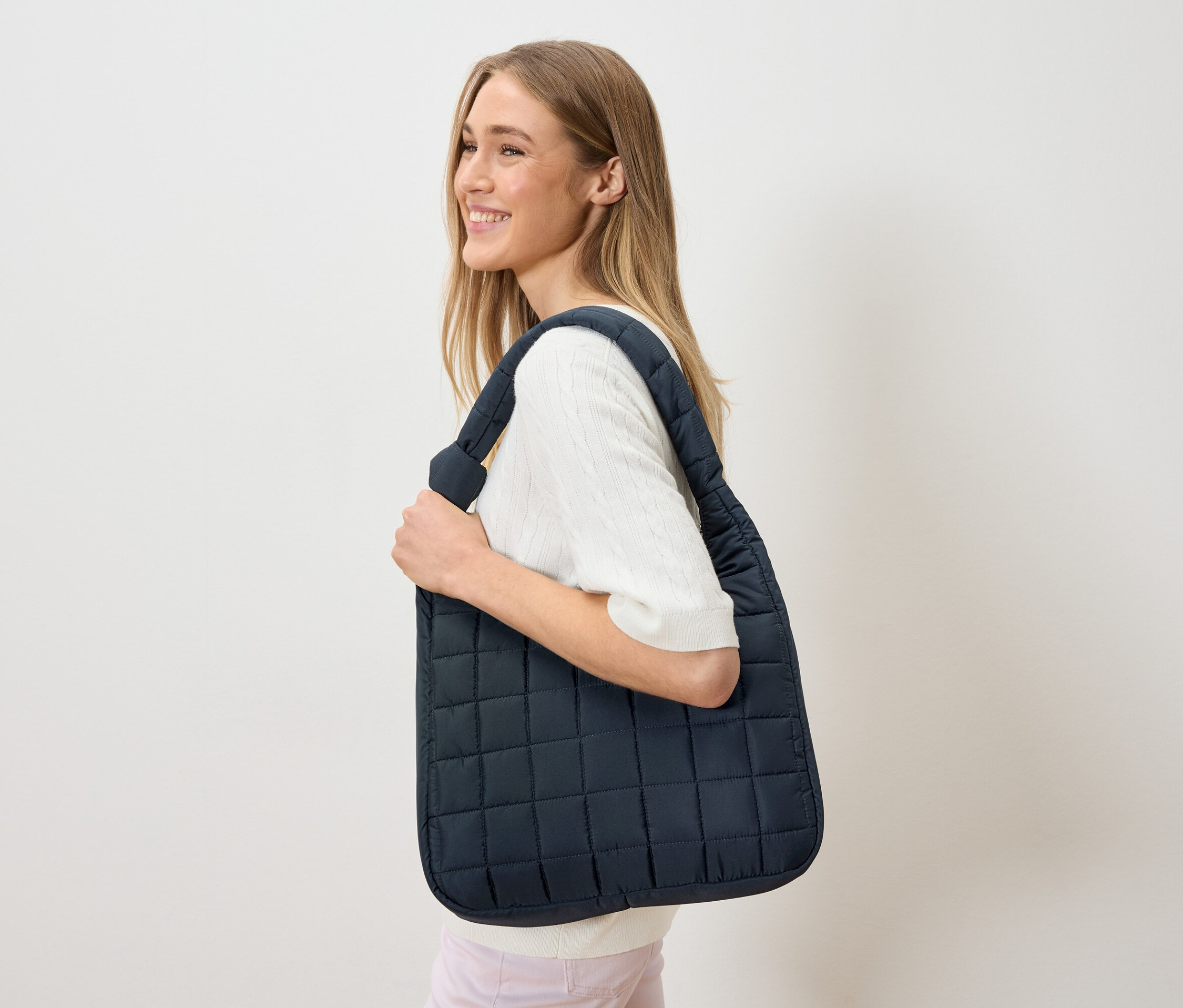 Une femme porte un sac fourre-tout matelassé bleu marine sur l'épaule.