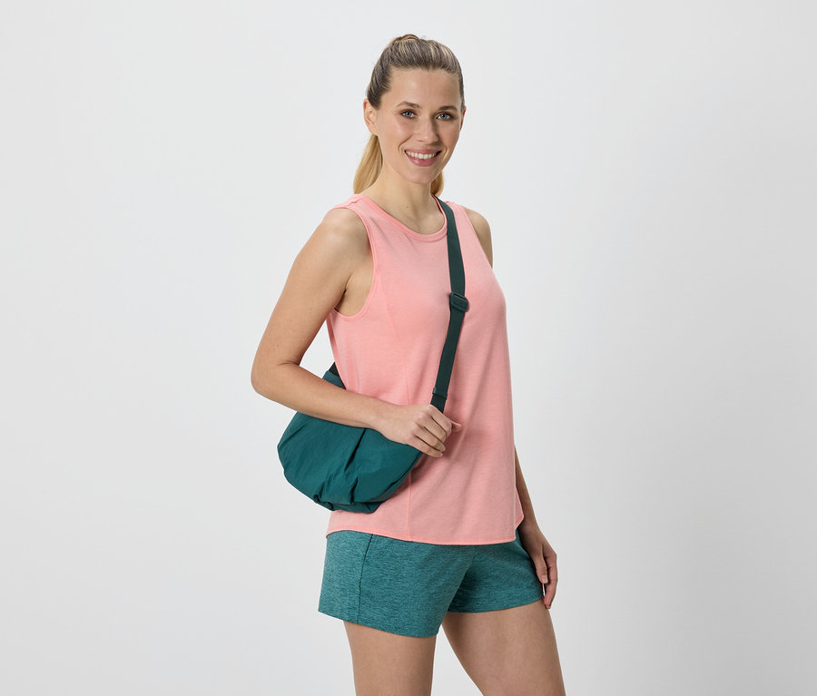 Femme avec un sac de marin vert sur l'épaule, vêtue d'un débardeur rose et d'un short vert.