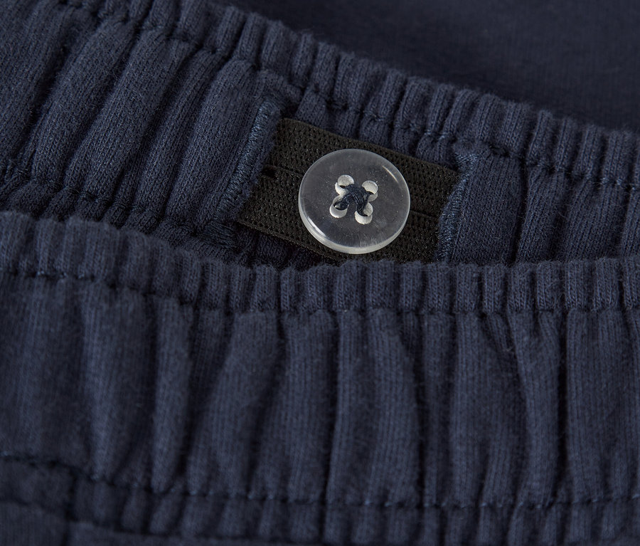 Gros plan d'un pantalon en tissu bleu marine avec une taille élastique et un détail de bouton réglable.