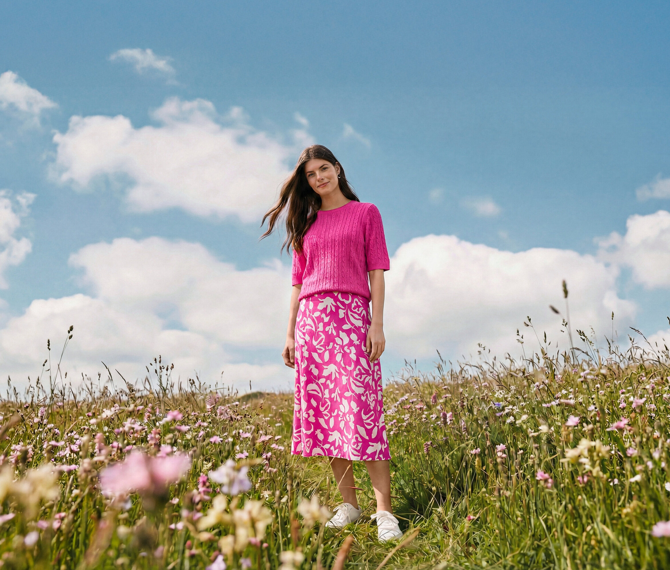 Une femme se tient dans un champ portant une jupe midi imprimée, des créoles vague et des baskets en cuir.