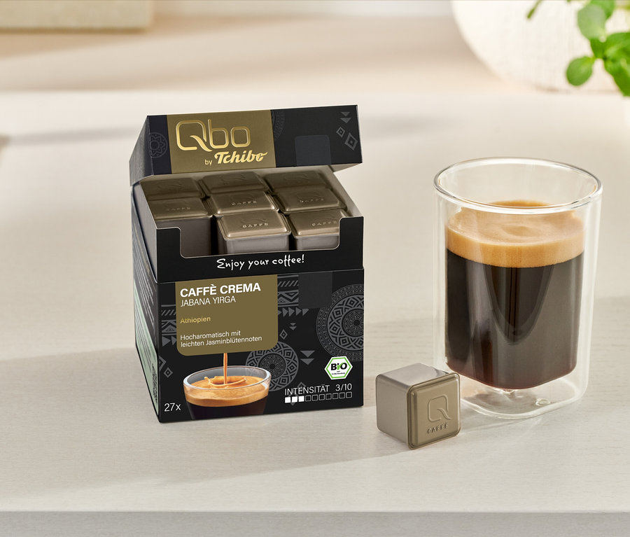 Boîte ouverte de Qbo Caffè Jabana Yirga avec des capsules, une tasse de café et une capsule individuelle sur une surface claire.