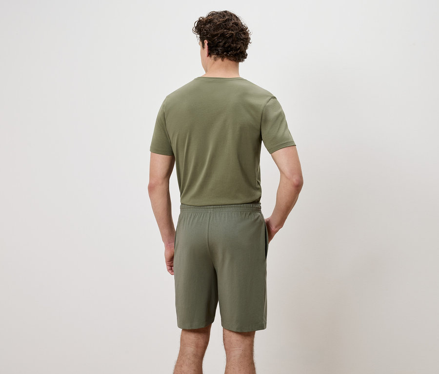 Vue arrière d'un homme portant un t-shirt et un short vert olive, les mains dans les poches.