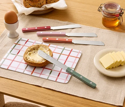 Sur une table, un pain beurré, quatre couteaux, du beurre, du miel, un œuf et du pain.