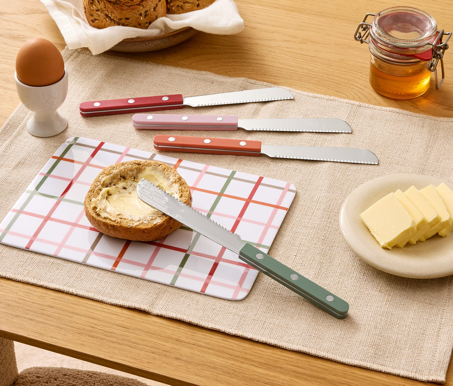 Sur une table, un pain beurré, quatre couteaux, du beurre, du miel, un œuf et du pain.