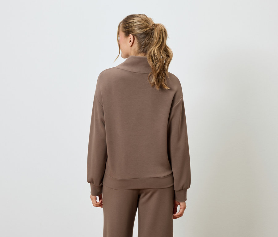 Vue de dos d'une femme blonde portant un pull marron et un pantalon marron.