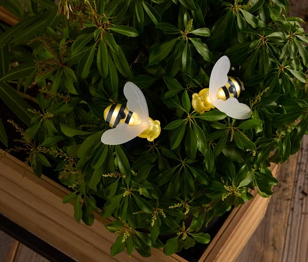Deux abeilles jaunes et noires à rayures avec des ailes translucides au milieu de feuilles vertes dans une boîte en bois.