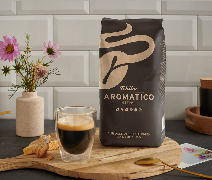 Une tasse de café est posée à côté d'un paquet de café en grains Aromatico Intenso - 1 kg sur une table en bois.