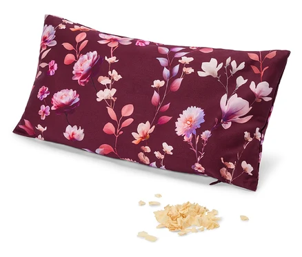 Un oreiller rectangulaire avec un fond rouge foncé et un motif floral de fleurs et de feuilles roses, violettes et blanches. À côté de l'oreiller se trouve un petit tas de matière légère et feuilletée.