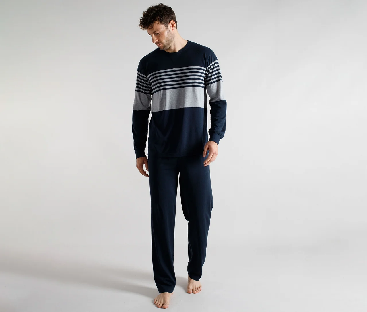 Homme portant un haut de pyjama à manches longues rayé bleu marine et gris et un pantalon de pyjama uni bleu marine, regardant vers le bas.