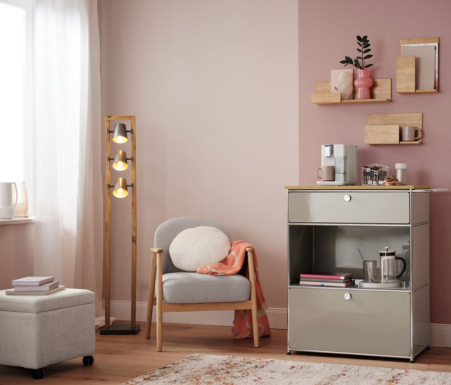 Salon avec fauteuil, lampe et commode avec machine à café. Sur la commode, un panier à capsules, blanc.