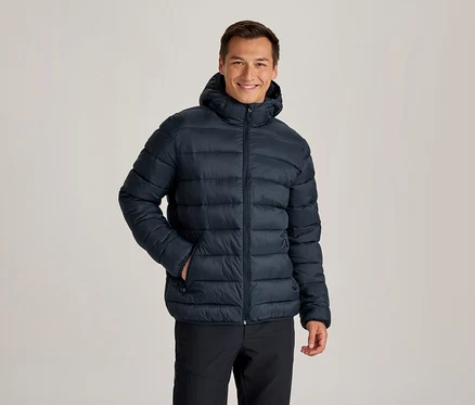 Homme souriant portant une doudoune à capuche bleu foncé et un pantalon noir, une main dans la poche de sa veste.