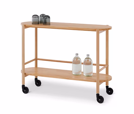 Un chariot de service ovale en bois clair avec deux étagères. Trois verres foncés retournés sont sur l'étagère supérieure, et deux bouteilles d'eau sur l'étagère inférieure. Le chariot a des roulettes noires.