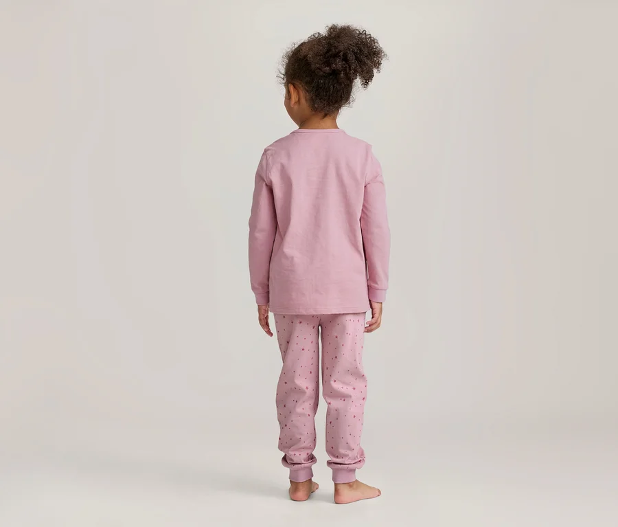 Jeune fille vue de dos, portant un pyjama rose à manches longues avec un pantalon à motifs, pieds nus devant un fond clair.