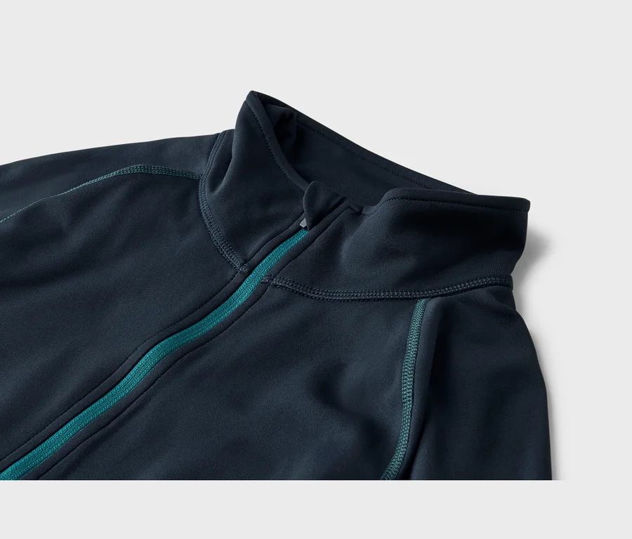 Gros plan d'une veste bleu foncé à col montant, avec une fermeture éclair turquoise sur le devant et des coutures turquoise.