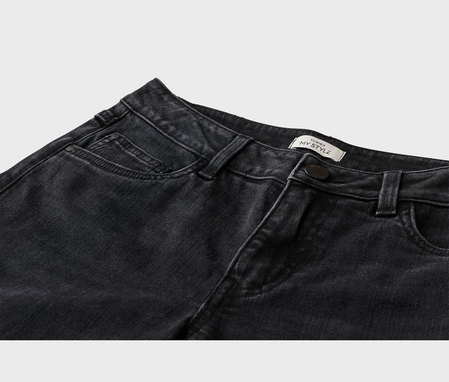 Gros plan sur la partie supérieure d'un jean noir, montrant une poche avant, des passants de ceinture, un bouton foncé et une étiquette blanche « TCHIBO MY STYLE » sur la ceinture.