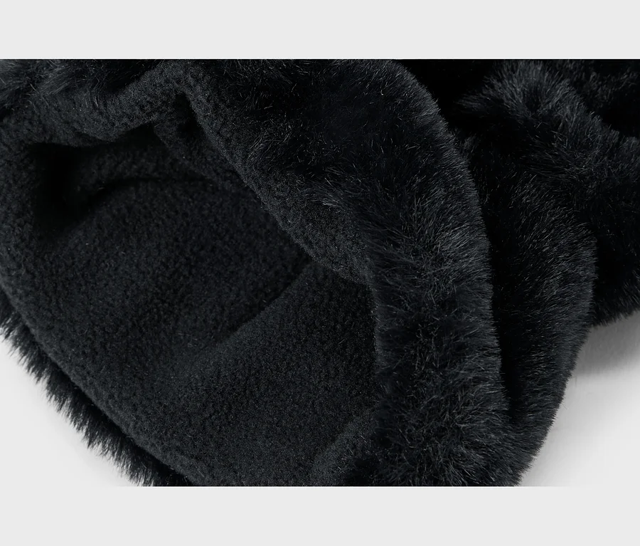 Gros plan d'un tissu noir plié, montrant un côté en fausse fourrure duveteuse et un côté intérieur plus doux et tricoté.
