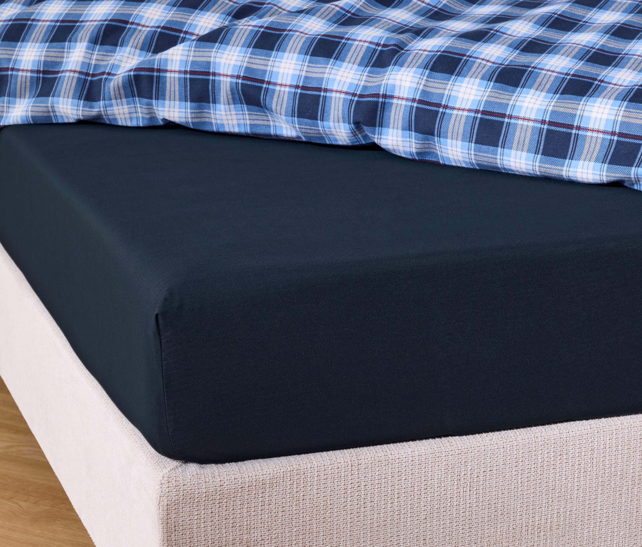 Gros plan d'un drap-housse bleu marine sur un lit avec une couverture à carreaux bleu et blanc.